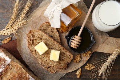 Photo of Slices of bread with butter, honey, milk and walnuts on wooden table, flat lay