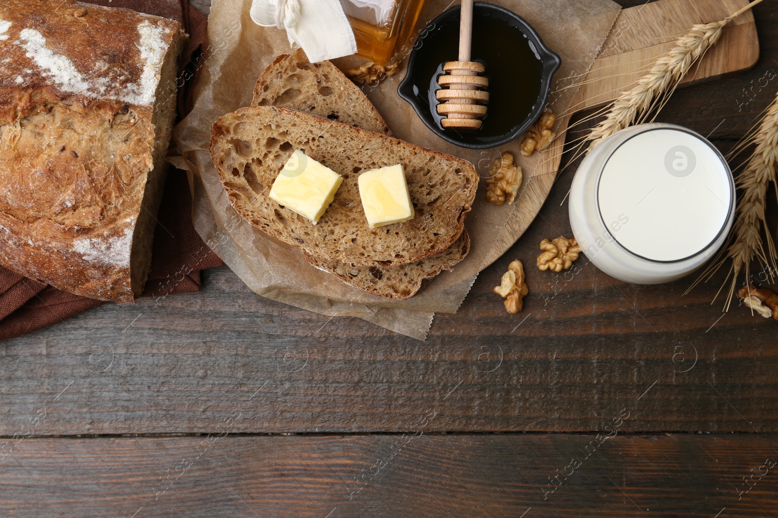 Photo of Slices of bread with butter, honey, milk and walnuts on wooden table, flat lay. Space for text