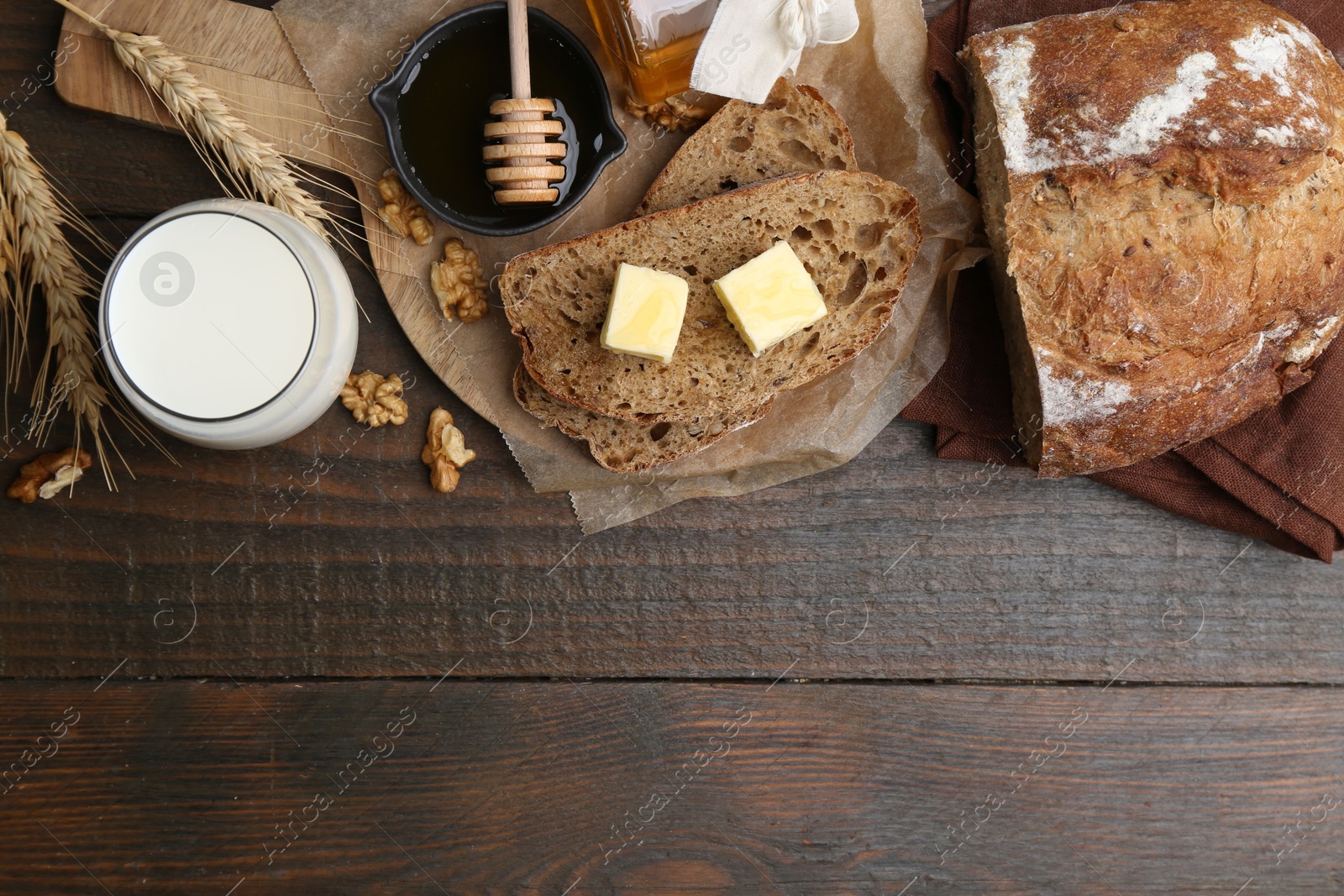 Photo of Slices of bread with butter, honey, milk and walnuts on wooden table, flat lay. Space for text