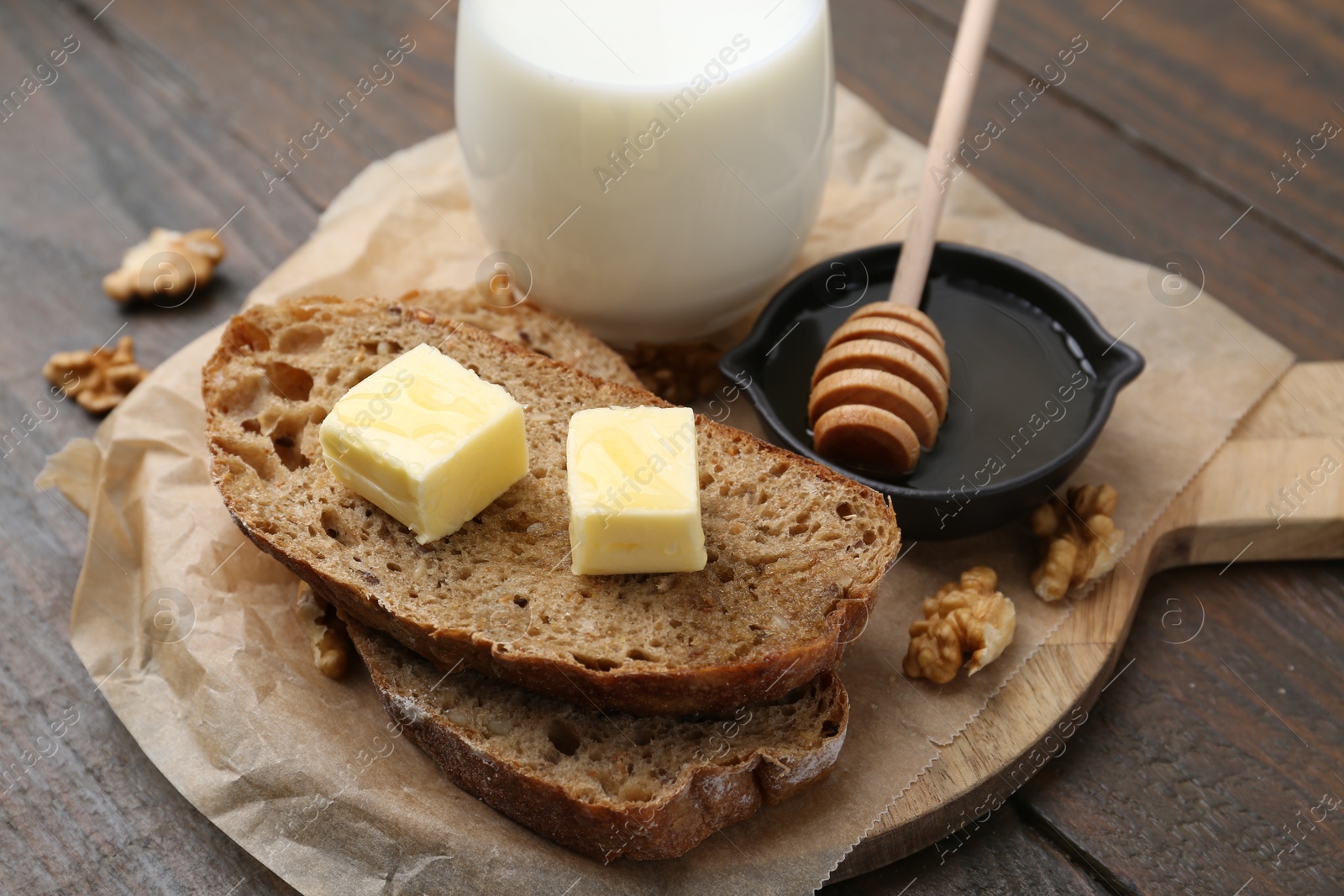 Photo of Slices of bread with butter, honey, milk and walnuts on wooden table, closeup