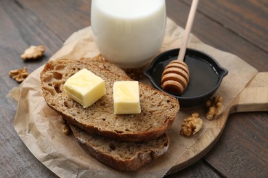 Photo of Slices of bread with butter, honey, milk and walnuts on wooden table, closeup