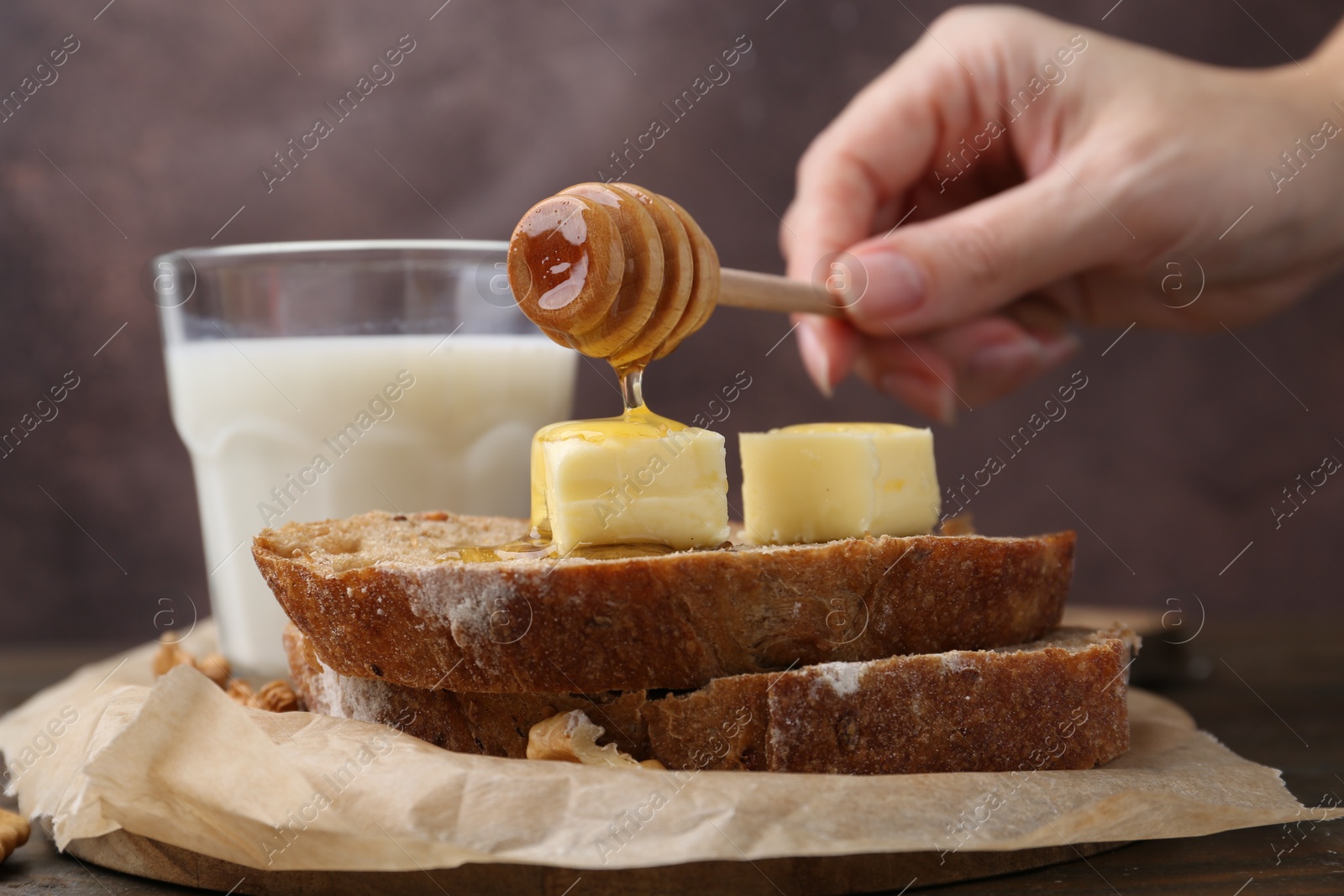 Photo of Woman pouring honey onto slices of bread with butter at wooden table, closeup