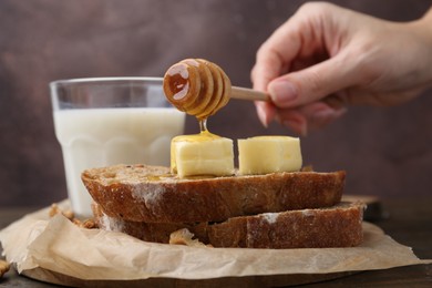 Woman pouring honey onto slices of bread with butter at wooden table, closeup