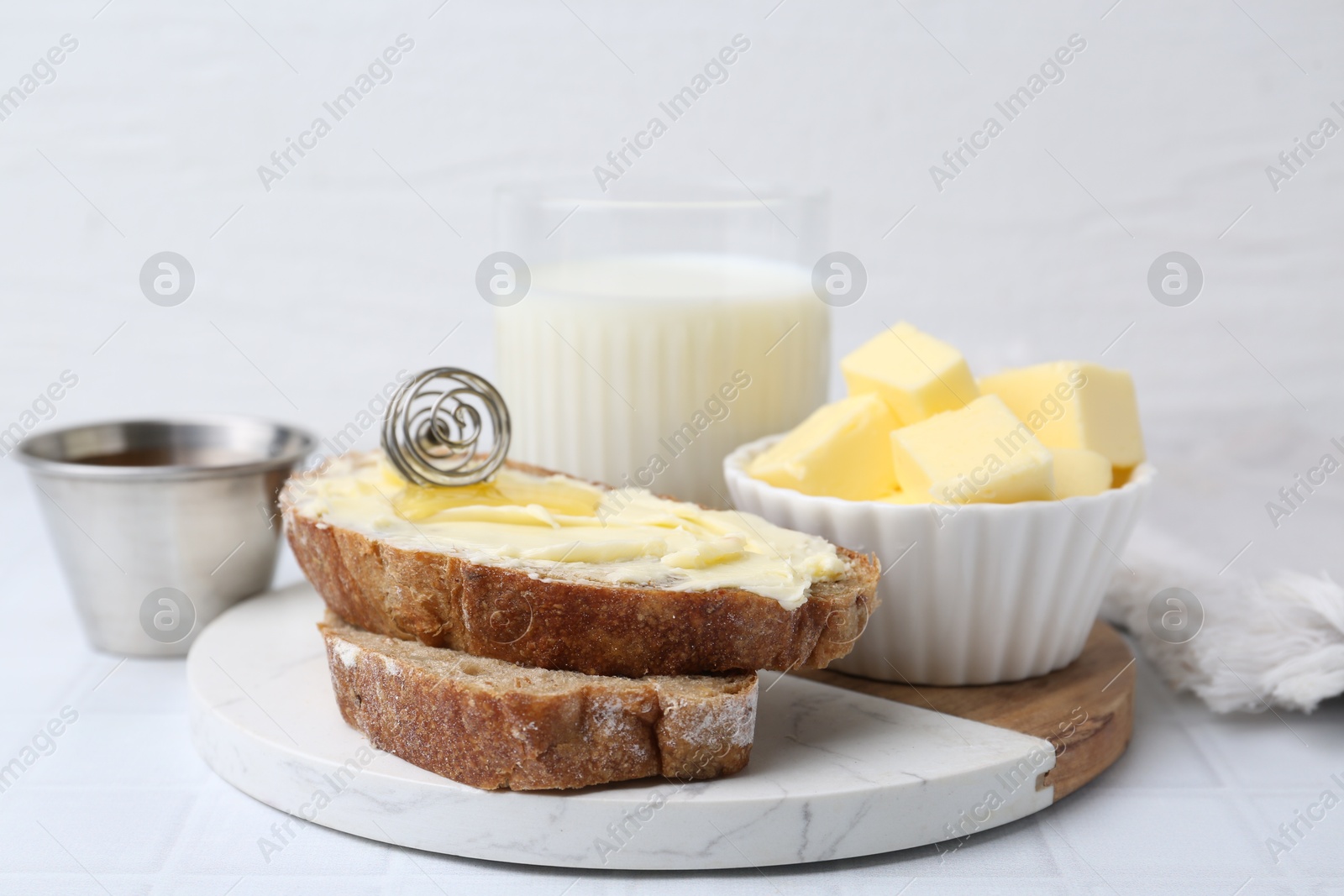 Photo of Slices of bread with butter, honey and milk on white tiled table, closeup