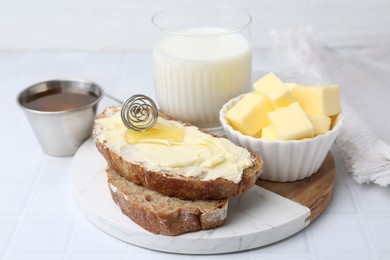 Photo of Slices of bread with butter, honey and milk on white tiled table, closeup