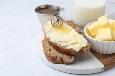 Photo of Slices of bread with butter, honey and milk on white tiled table, closeup. Space for text