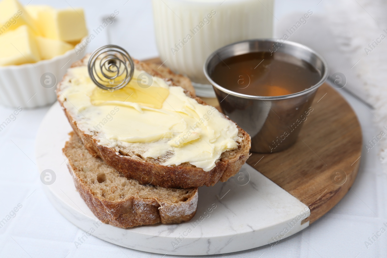 Photo of Slices of bread with butter, honey and milk on white tiled table, closeup