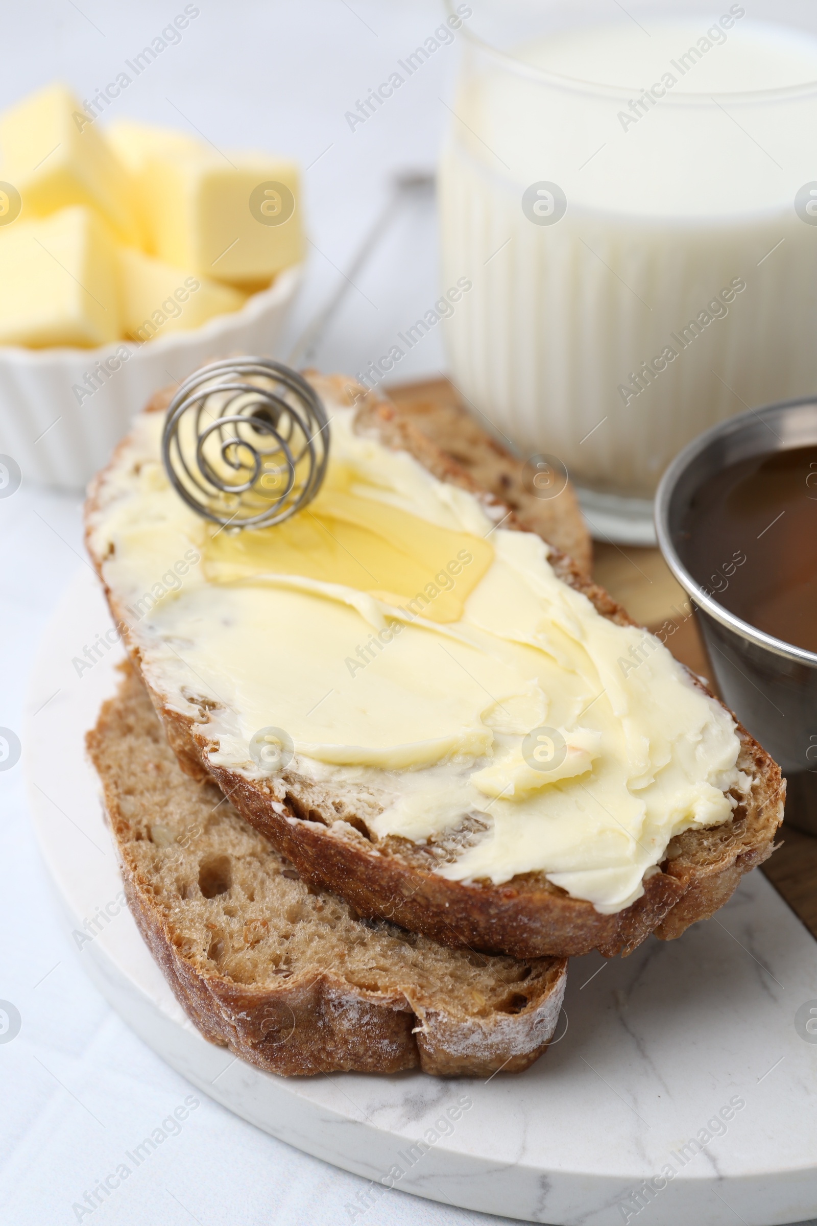 Photo of Slices of bread with butter, honey and milk on white table, closeup