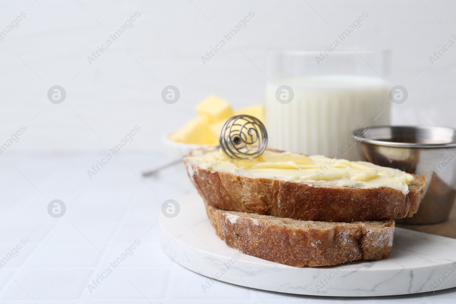 Photo of Slices of bread with butter, honey and milk on white tiled table, closeup. Space for text