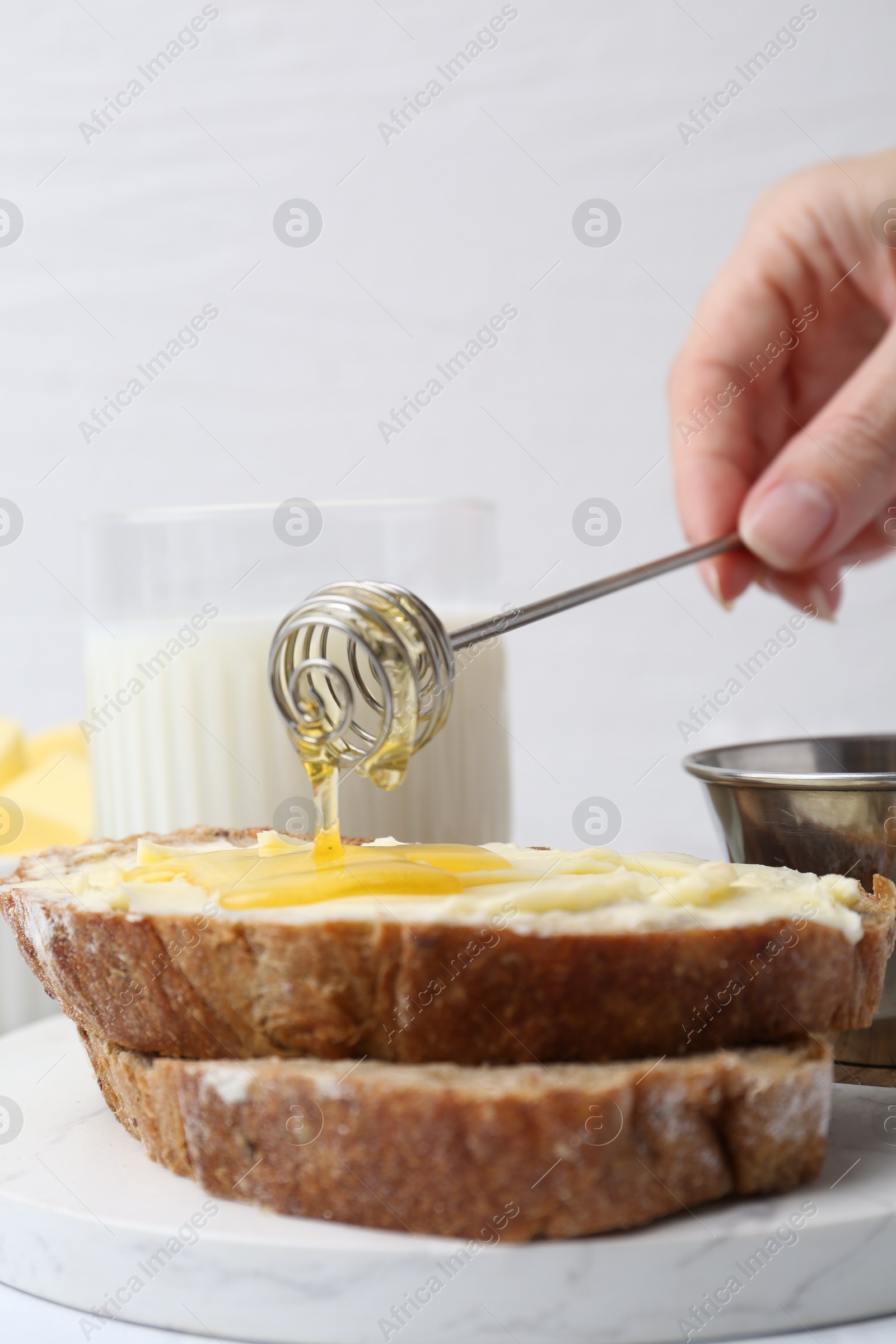 Photo of Woman pouring honey onto slices of bread with butter at white table, closeup