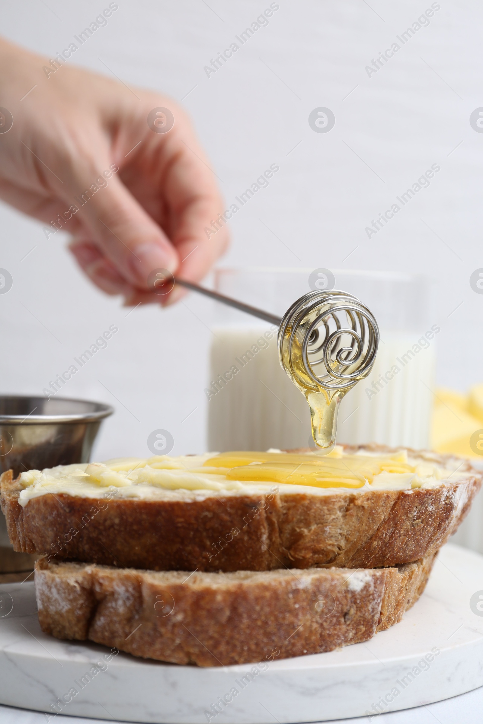 Photo of Woman pouring honey onto slices of bread with butter at white table, closeup