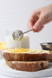 Woman pouring honey onto slices of bread with butter at white table, closeup