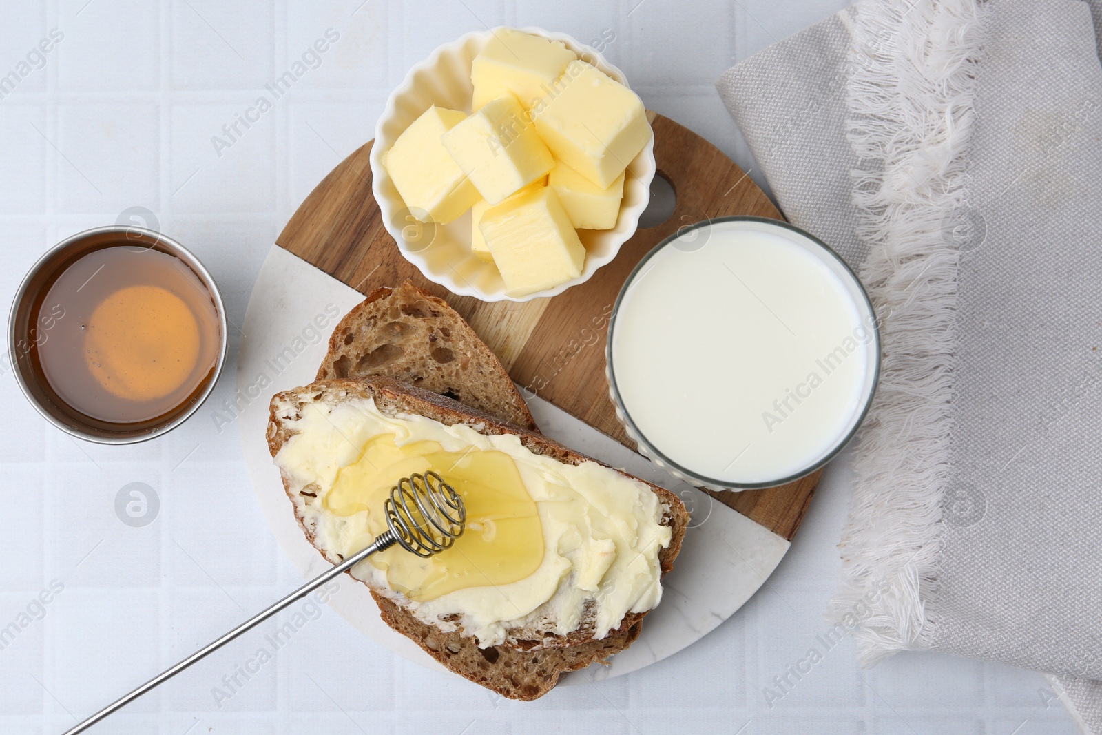 Photo of Slices of bread with butter, honey and milk on white tiled table, flat lay