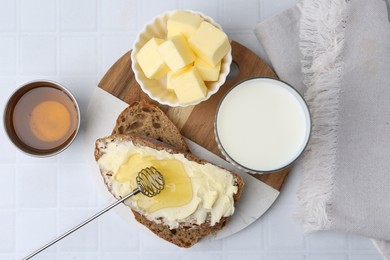 Photo of Slices of bread with butter, honey and milk on white tiled table, flat lay