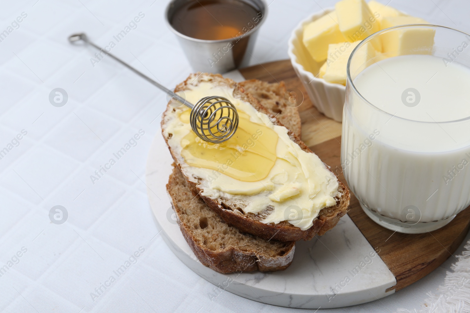 Photo of Slices of bread with butter, honey and milk on white tiled table, closeup. Space for text