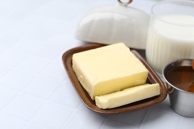 Fresh milk in glass, honey and butter on white tiled table, closeup. Space for text