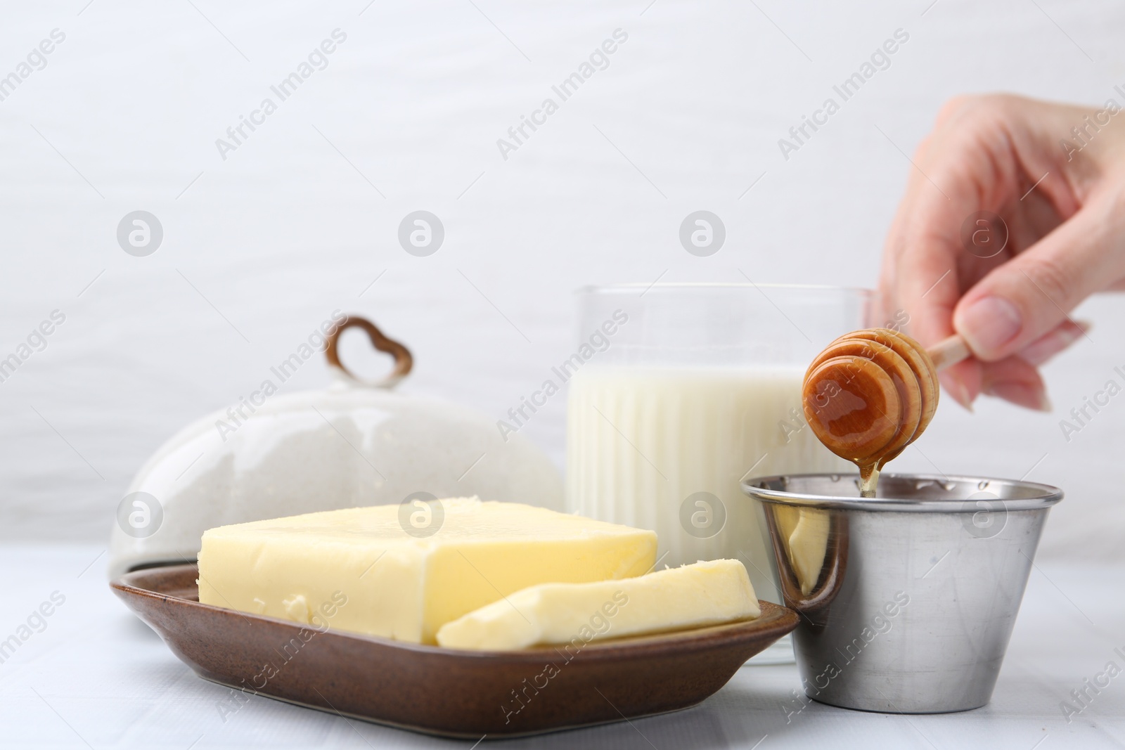 Photo of Woman with honey dipper, closeup. Fresh milk in glass and butter on white tiled table