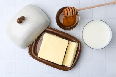 Photo of Fresh milk in glass, honey and butter on white tiled table, flat lay