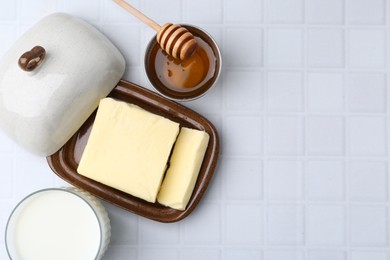 Photo of Fresh milk in glass, honey and butter on white tiled table, flat lay. Space for text