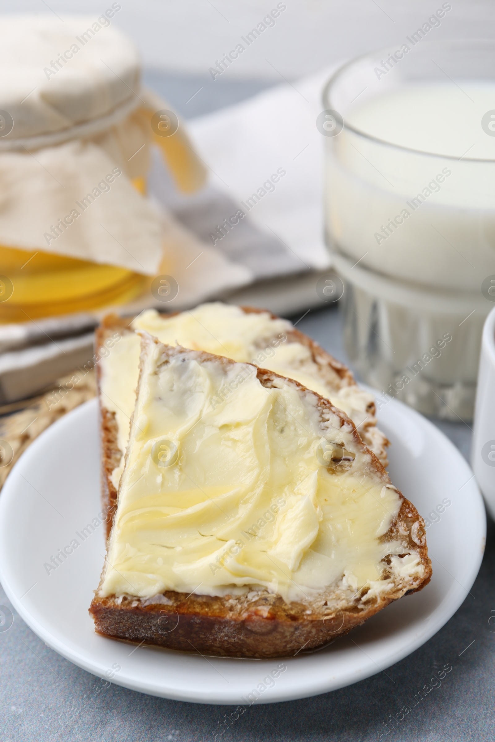 Photo of Slices of bread with butter, honey and milk on light grey table, closeup