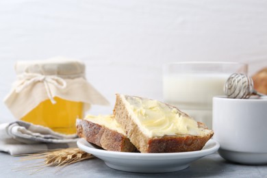 Photo of Slices of bread with butter, honey, milk and spike on light grey table, closeup