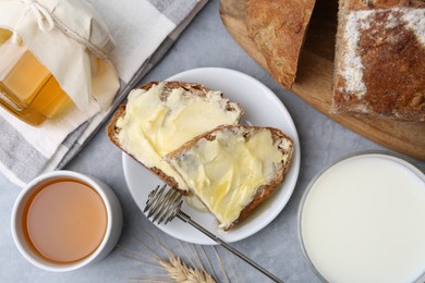 Photo of Slices of bread with butter, honey and milk on grey table, flat lay