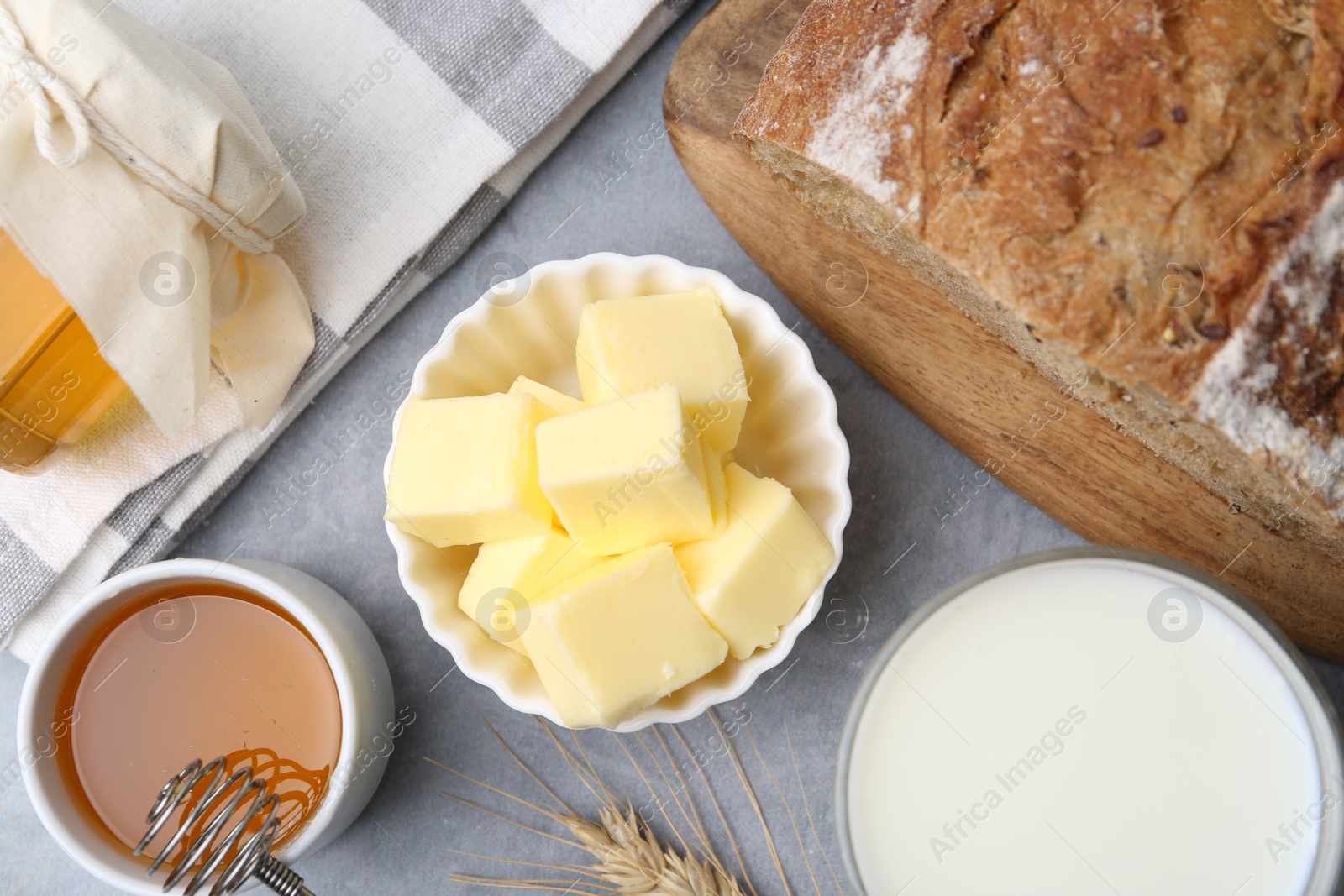 Photo of Fresh butter, milk, honey and bread on grey table, flat lay