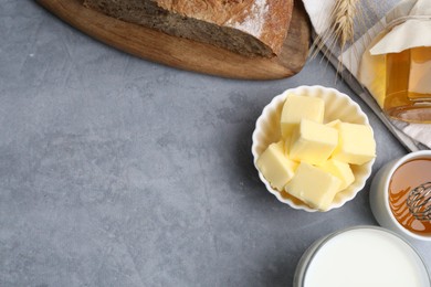 Photo of Fresh butter, milk, honey and bread on grey table, flat lay. Space for text