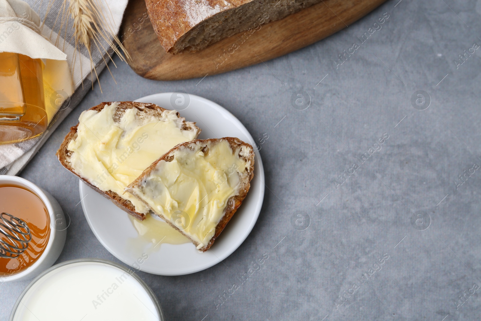 Photo of Slices of bread with butter, honey and milk on grey table, flat lay. Space for text