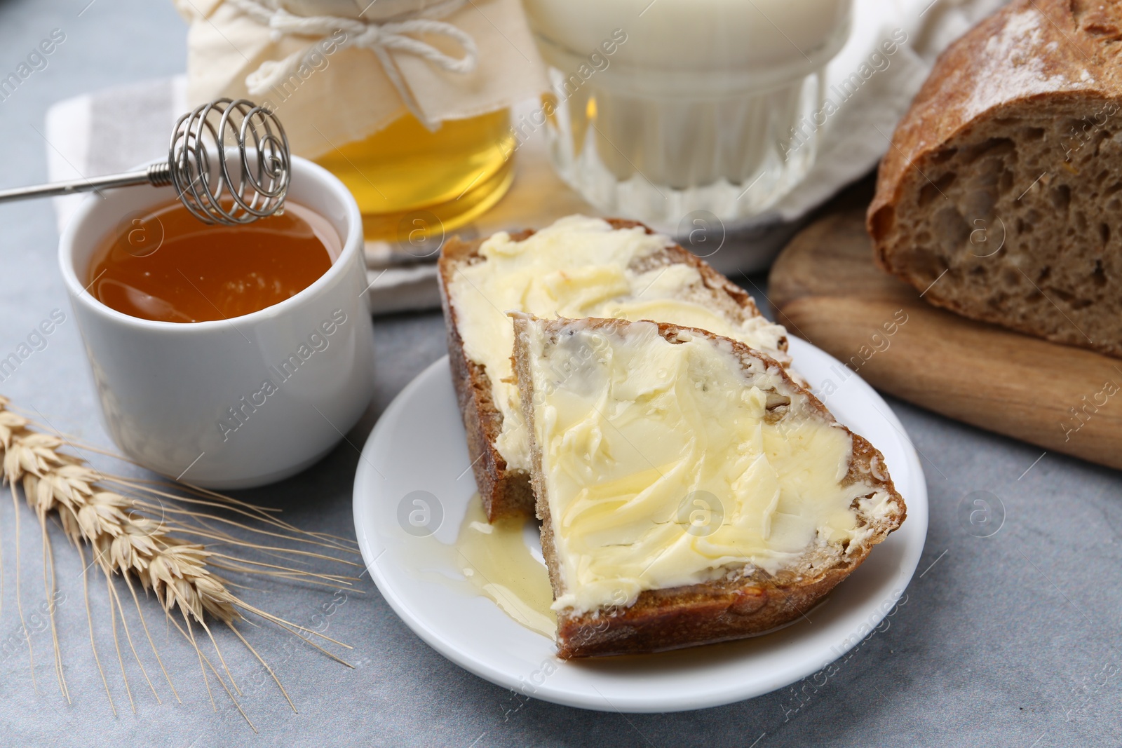 Photo of Slices of bread with butter, honey and milk on grey table, closeup