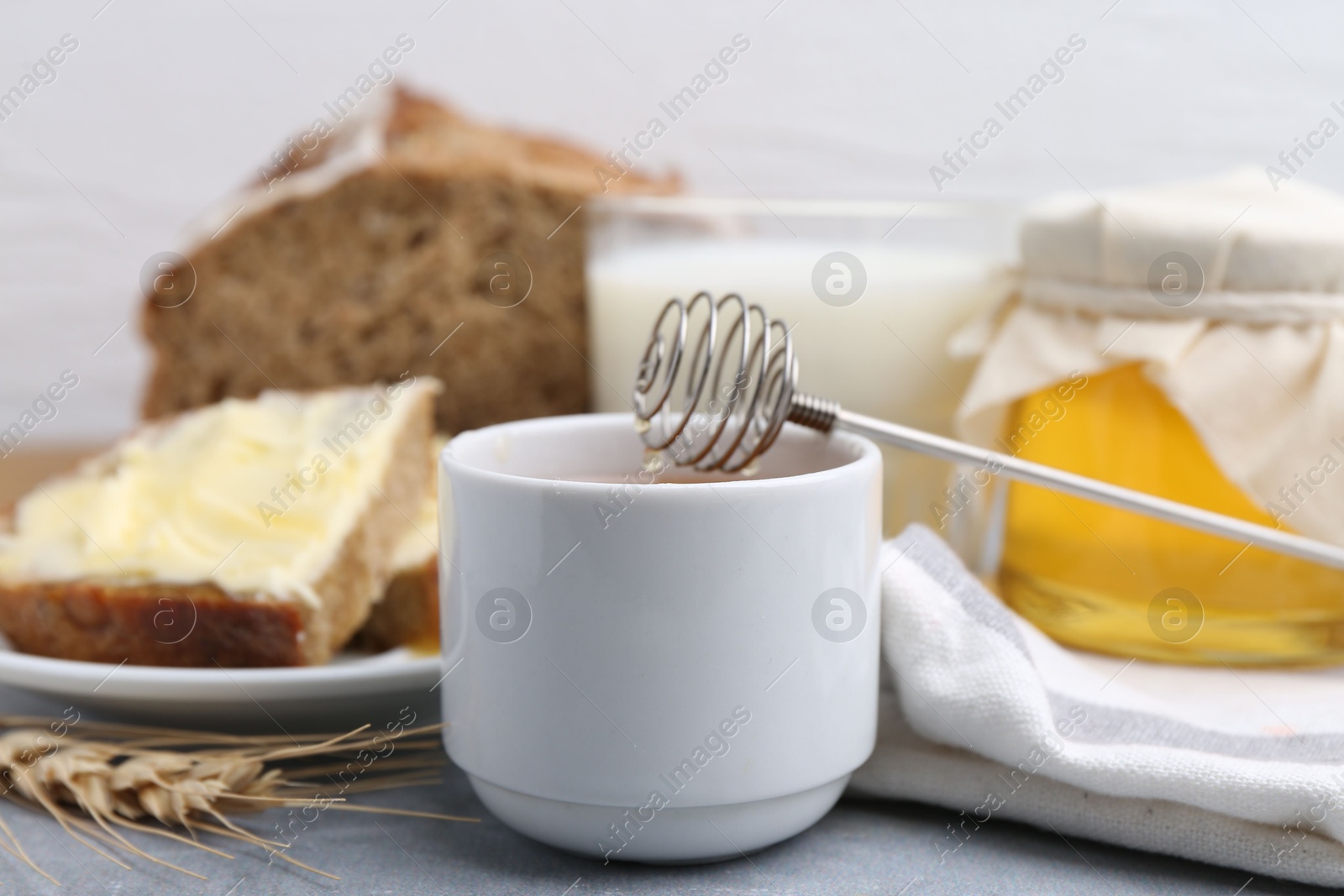 Photo of Honey, milk and bread on grey table, closeup