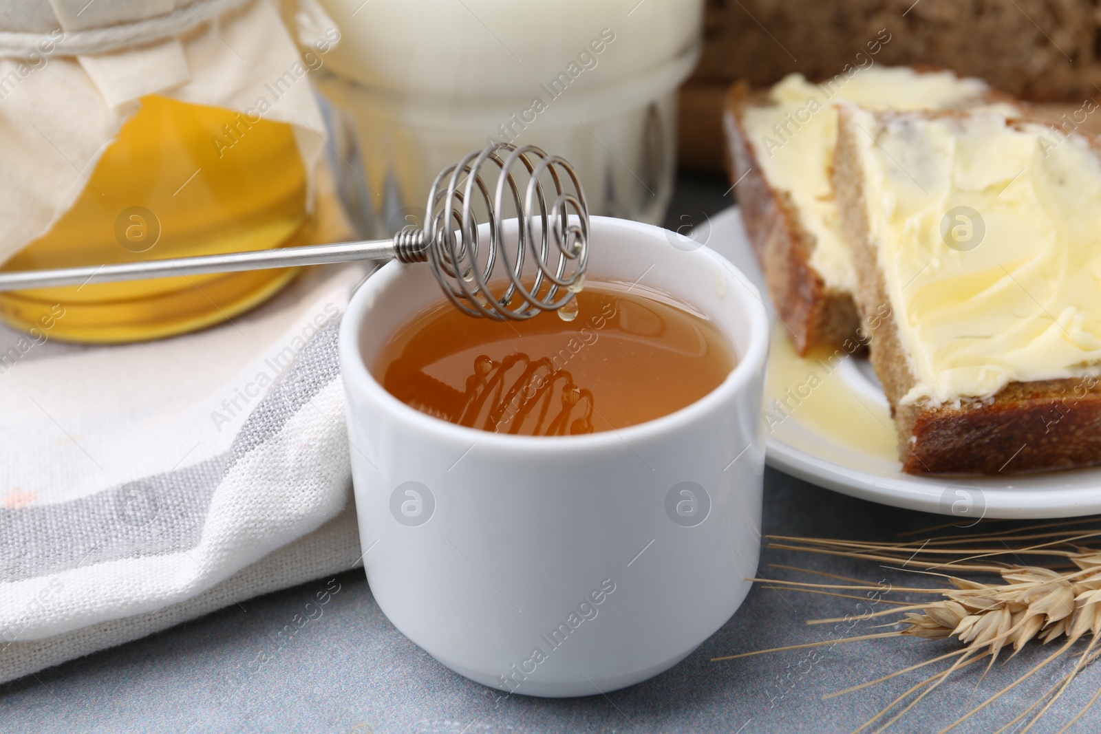 Photo of Slices of bread with butter, honey, milk and spike on grey table, closeup