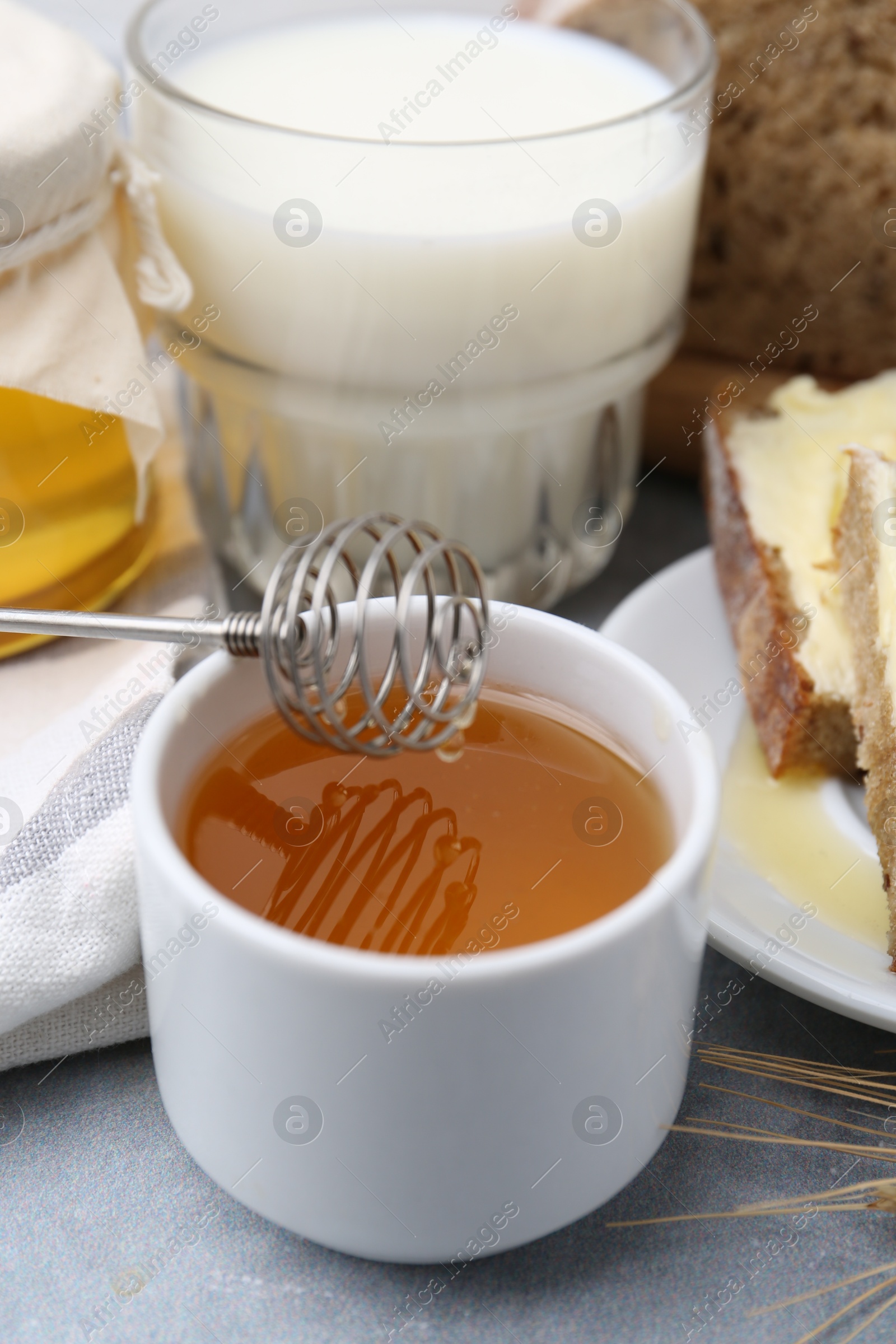 Photo of Honey, milk and bread on grey table, closeup