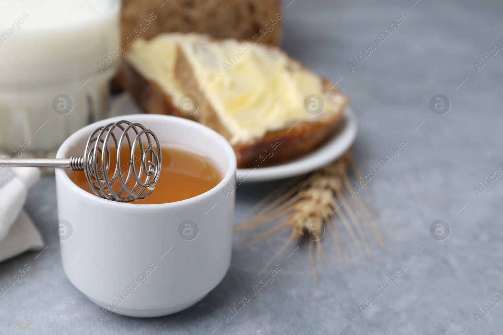 Photo of Honey, milk and bread slices with butter on grey table, closeup. Space for text