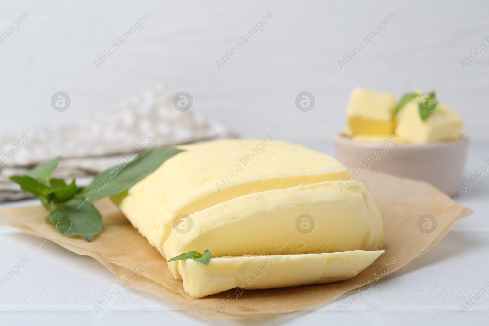 Photo of Cut brick of butter and basil on white tiled table, closeup