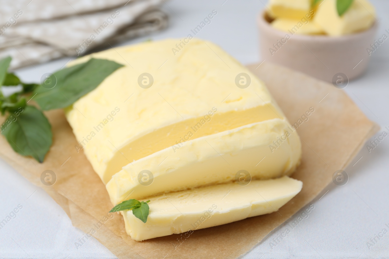 Photo of Cut brick of butter and basil on white table, closeup