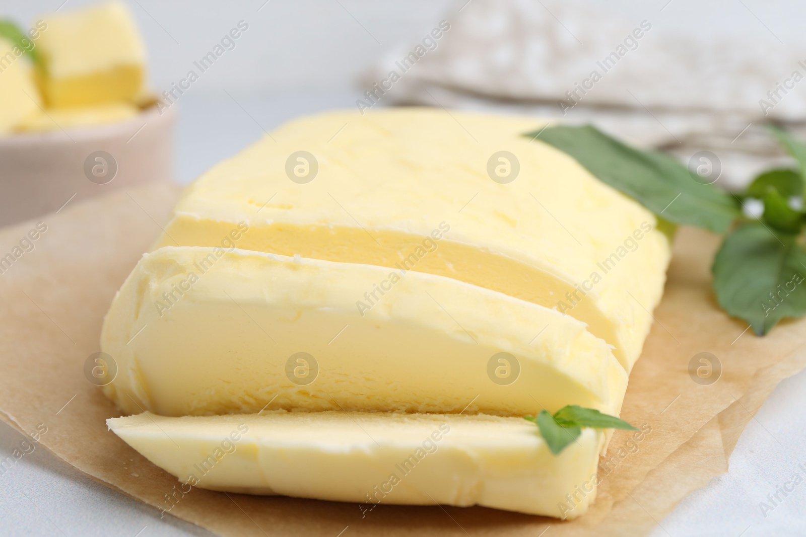 Photo of Cut brick of butter and basil on white table, closeup