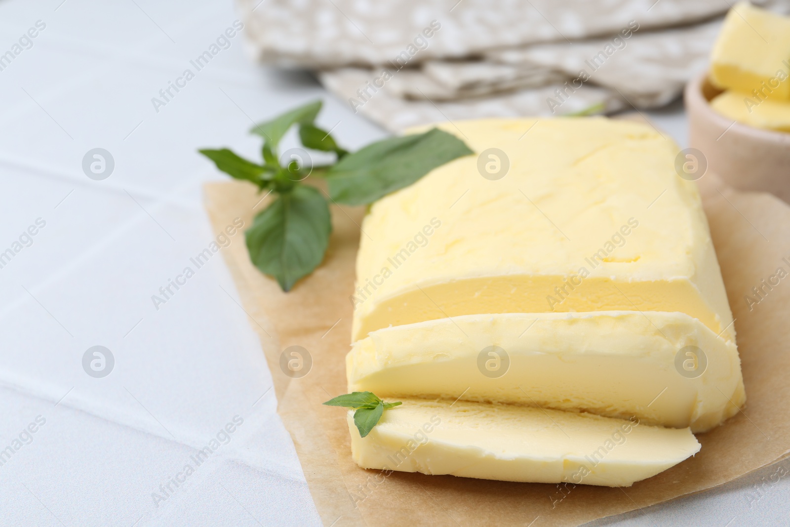 Photo of Cut brick of butter and basil on white tiled table, closeup. Space for text