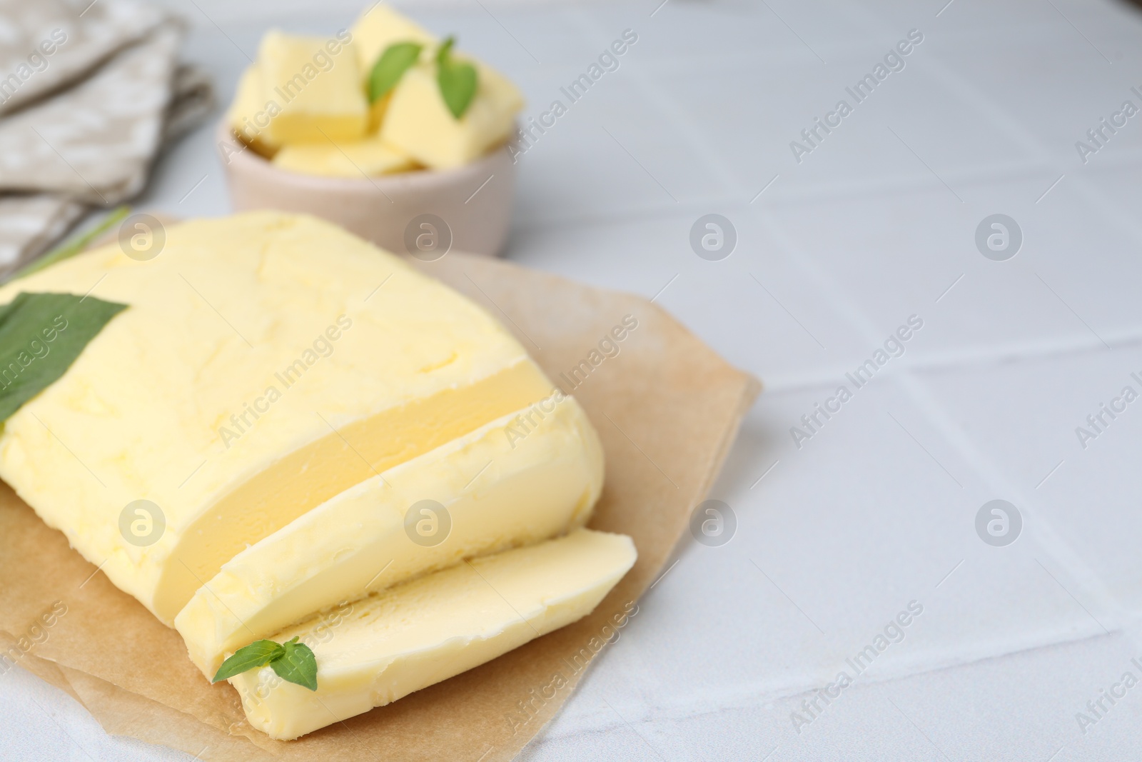 Photo of Cut butter and basil on white tiled table, closeup. Space for text