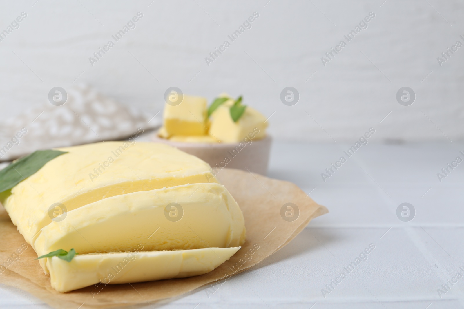 Photo of Cut butter and basil on white tiled table, closeup. Space for text