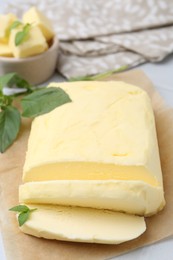 Photo of Cut brick of butter and basil on white table, closeup