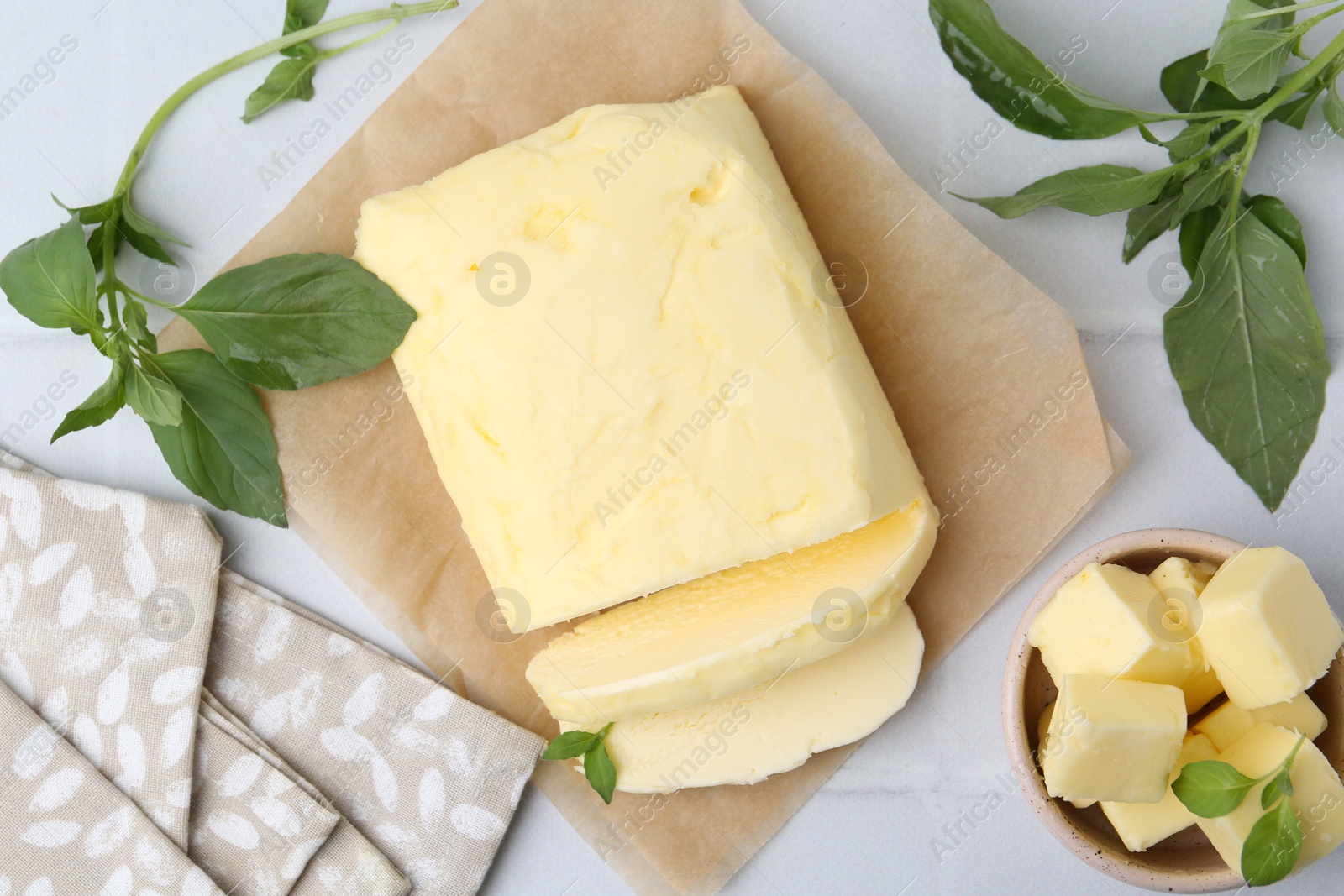 Photo of Cut butter and basil on white tiled table, flat lay