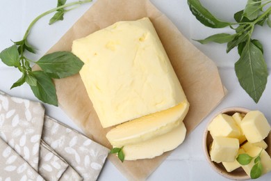 Photo of Cut butter and basil on white tiled table, flat lay