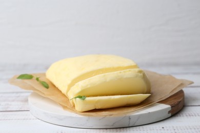 Photo of Cut brick of butter and basil on white wooden table, closeup. Space for text