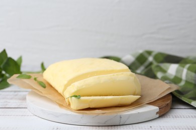 Photo of Cut brick of butter and basil on white wooden table, closeup. Space for text