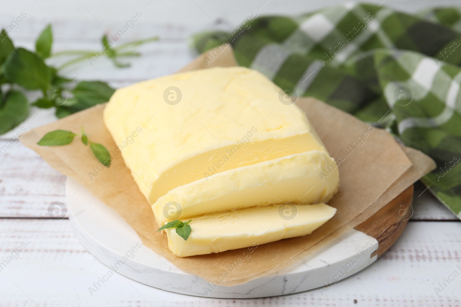 Photo of Cut brick of butter and basil on white wooden table, closeup