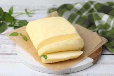 Photo of Cut brick of butter and basil on white wooden table, closeup