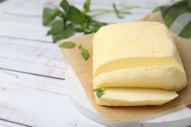 Cut brick of butter and basil on white wooden table, closeup. Space for text