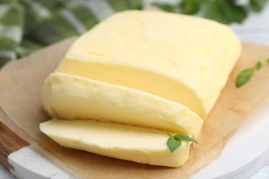 Photo of Cut brick of butter and basil on table, closeup