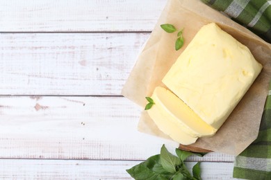 Photo of Cut brick of butter and basil on white wooden table, flat lay. Space for text